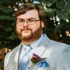 Tyler Baker, a bearded man with glasses in a suit jacked